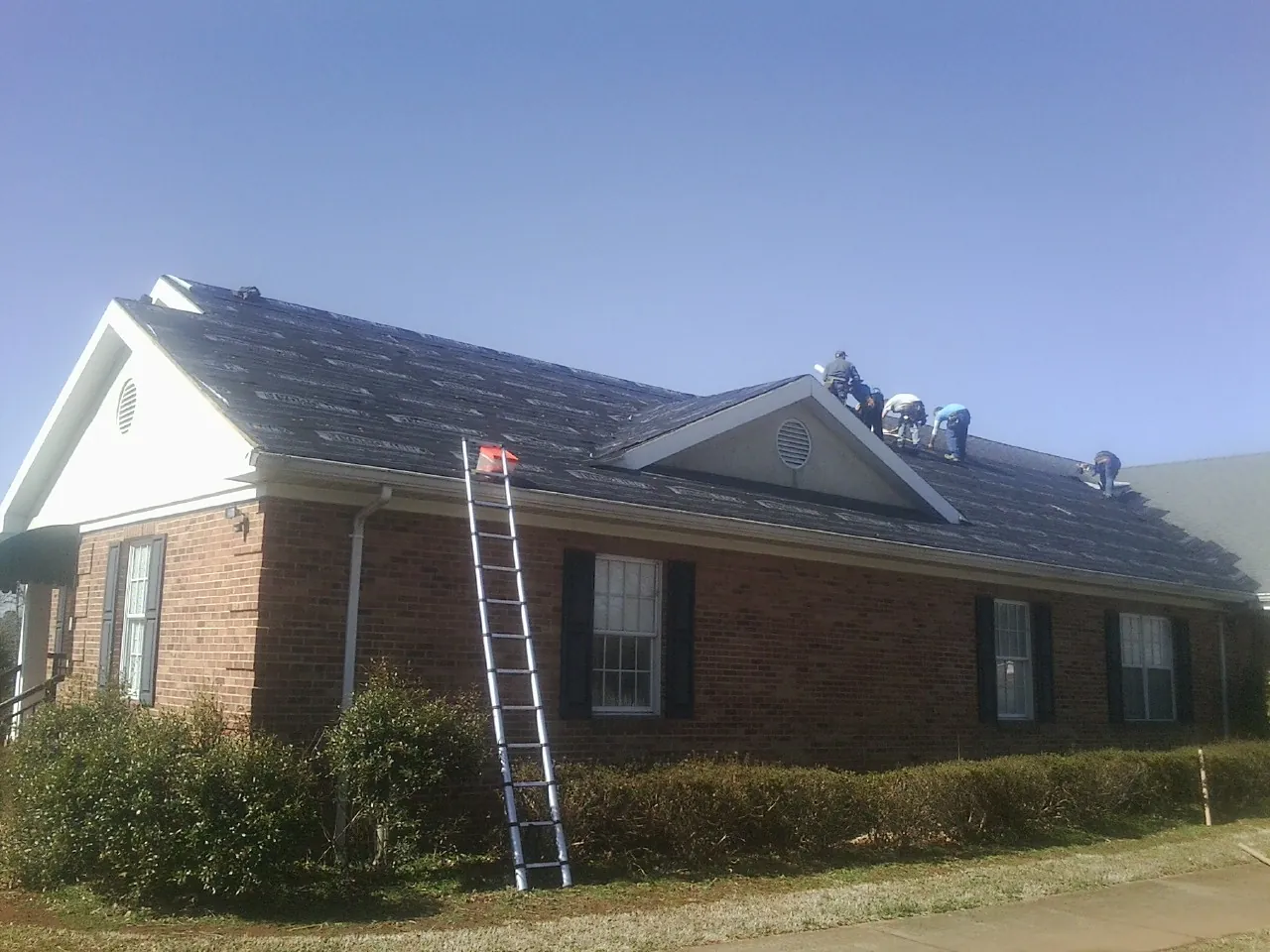 Crew tearing shingles off a brick ranch roof with a ladder set — Metal Roof Repair work by our crew in Cresskill