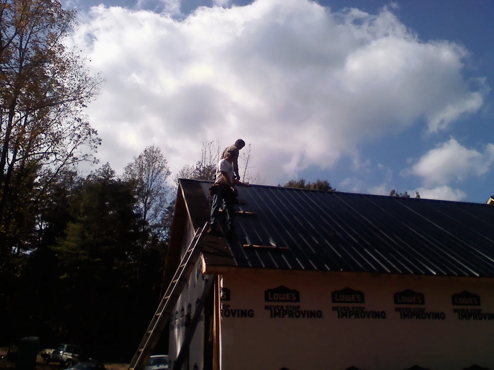 Roofer fastening dark metal panels high against a cloudy sky, from a Roof Inspection job in Cresskill